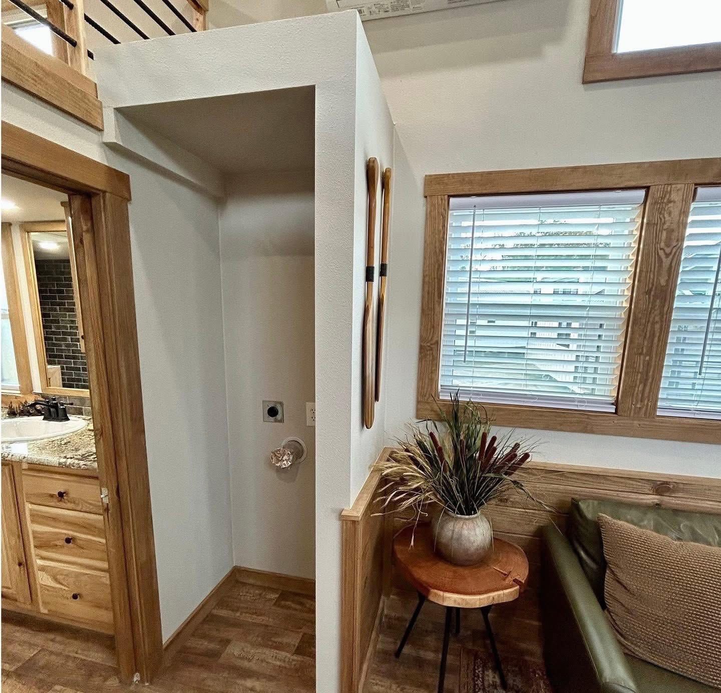 Cozy interior with wooden accents, featuring a small nook with light walls and decor paddles. A vase with dried plants sits on a table by a window.
