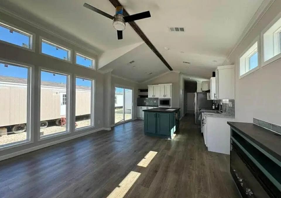 Spacious, modern kitchen and living area with large windows, wood floor, and vaulted ceiling. Light streams in, creating an airy, inviting atmosphere.