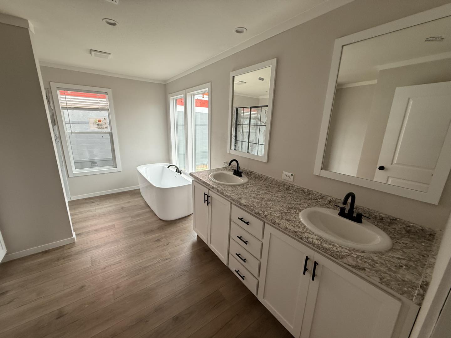Modern bathroom with a freestanding white tub by large windows. Double sink vanity with marble countertop and black fixtures. Bright, clean, and elegant.