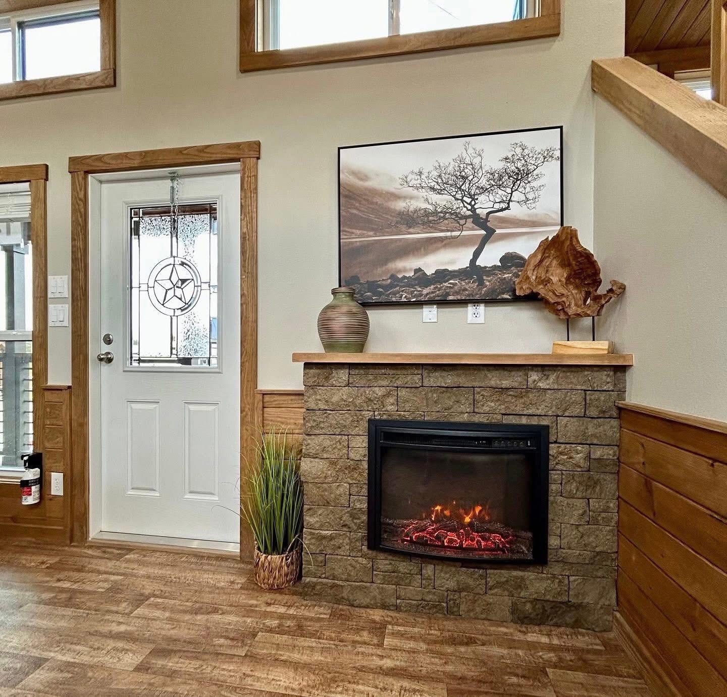 Cozy living space with a stone fireplace featuring a lit electric fire, wall art of a tree, wooden sculpture, and a decorative vase. Warm, inviting tone.