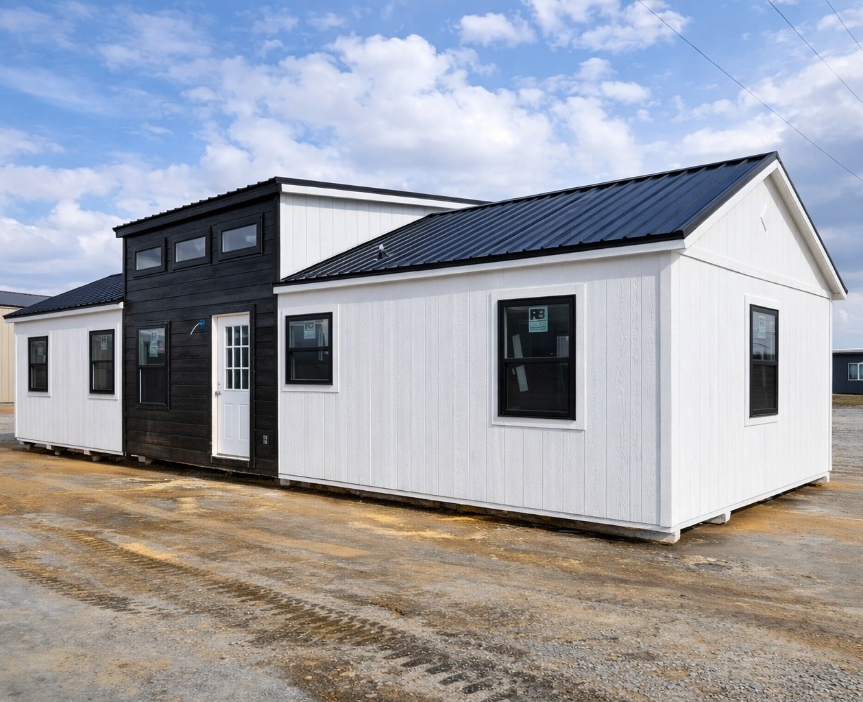 Modern tiny house with a black and white exterior, featuring a gabled roof and multiple windows, set on a sunny day with a cloudy blue sky.