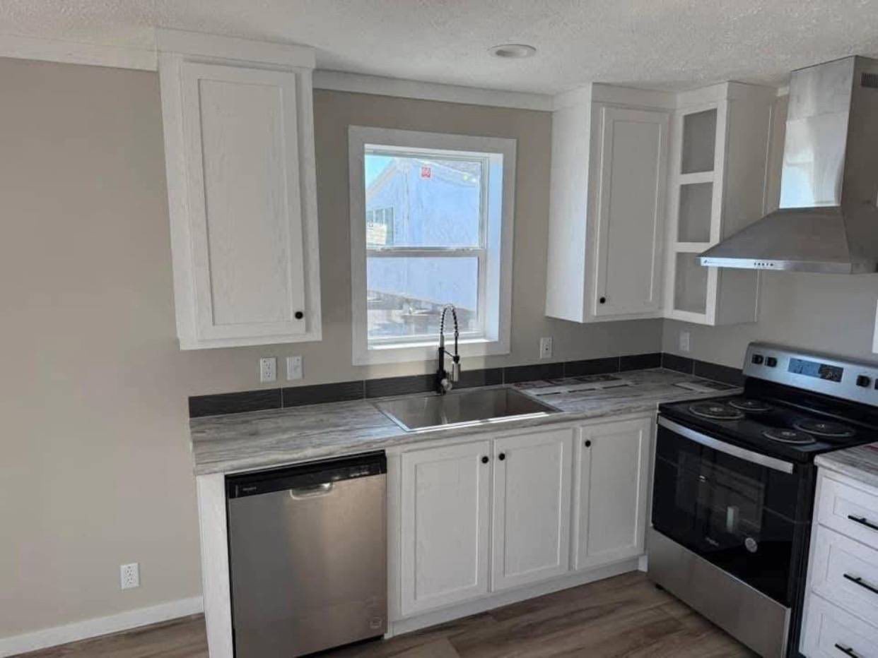 Modern kitchen with white cabinets and black handles. A stainless steel stove, dishwasher, and a sleek range hood. Large window above the sink.
