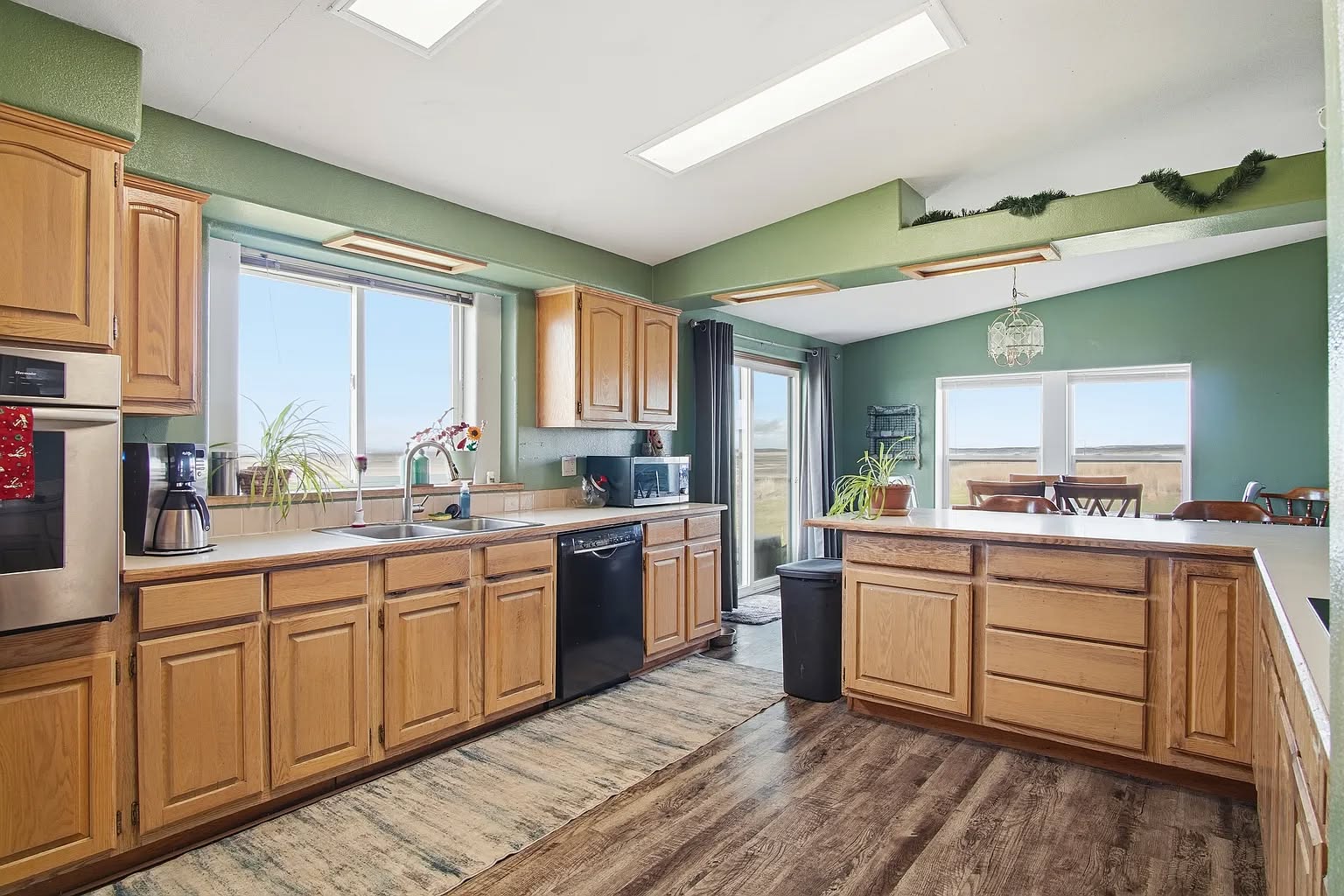 Spacious kitchen with light wood cabinets, black appliances, and green walls. Large windows and sliding door offer natural light and countryside views.