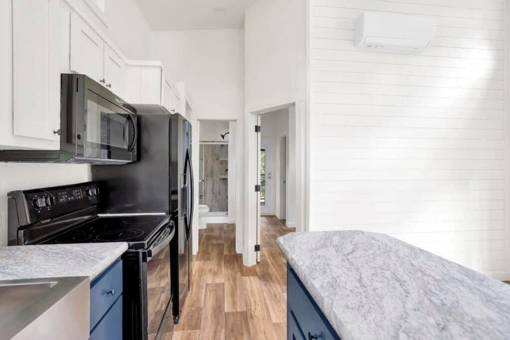 A modern kitchen with white cabinets, black appliances, and a wooden floor. Bright and airy with natural light on walls and a marble countertop.