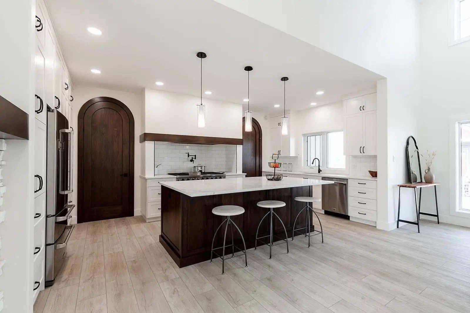 Spacious modern kitchen with a large island, dark wood accents, white cabinetry, pendant lights, and light wood flooring. Bright, airy, and sleek design.