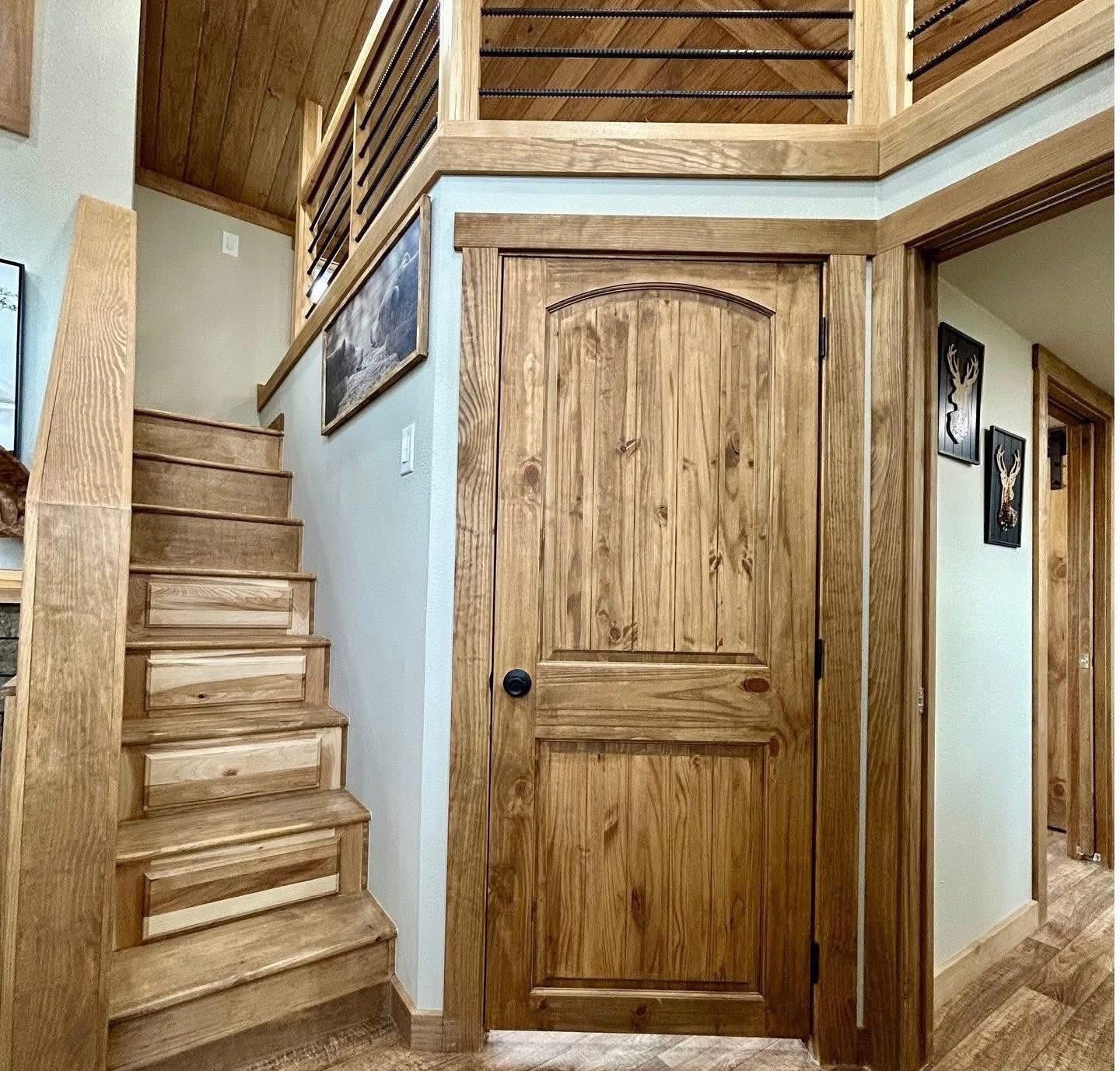 Warm, rustic interior with a wooden staircase leading up, featuring a wooden door on the right. The wood tones create a cozy ambiance.