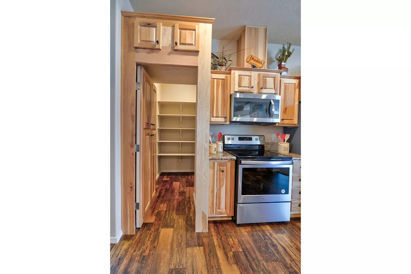 Cozy kitchen with wood cabinetry and hardwood floors, featuring a stainless steel oven. An open pantry with shelves is visible, conveying warmth and functionality.