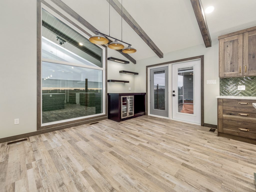 Modern dining room with wooden flooring, exposed beams, pendant lighting, large window with outdoor view, and French doors. Cozy and inviting.