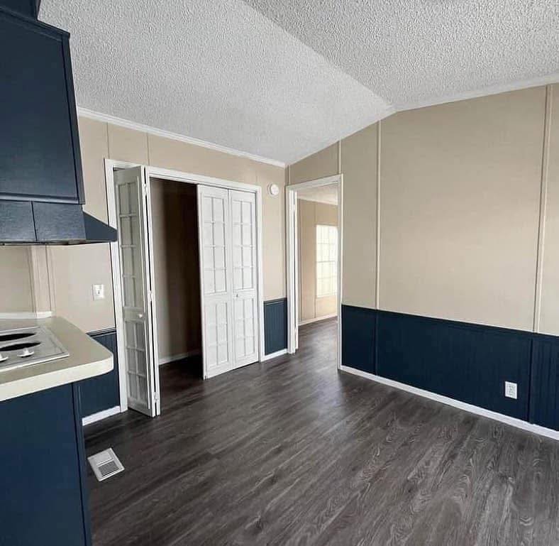 A minimalist room with dark wood flooring, beige walls, and blue wainscoting. A white door and bright light create a serene, clean ambiance.
