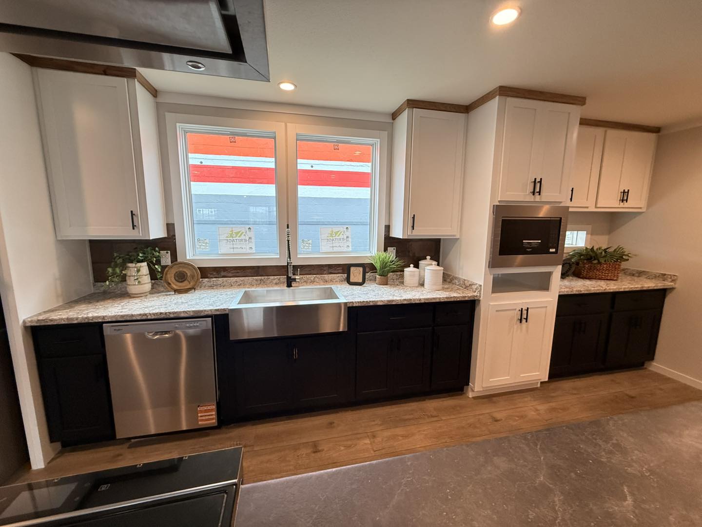 Modern kitchen with white upper and dark lower cabinets, granite countertops, and stainless steel appliances. Bright lighting and plants add warmth.
