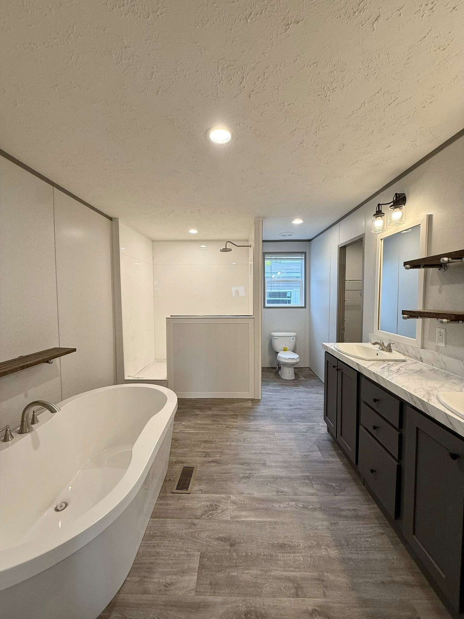 Modern bathroom with a freestanding bathtub, dual sinks on a marble countertop, and a separate shower area. Natural light from a window creates a clean, serene atmosphere.