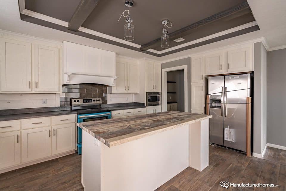 Modern kitchen with white cabinets, gray countertops, and a wooden island. Stainless steel appliances and two pendant lights add elegance. Cozy and inviting.