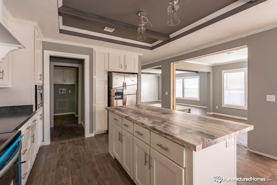 Modern kitchen with a large wooden island, white cabinets, and dark wood flooring. Gray ceiling with pendant lights adds a sleek touch. Bright and spacious.