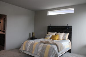 Modern bedroom with gray walls and a rectangular window. Bed features a dark headboard, floral and striped bedding, and yellow accent pillow, creating a cozy atmosphere.