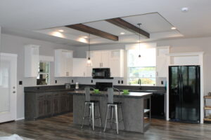 Modern kitchen with gray cabinets, white walls, and a black fridge. Pendant lights illuminate the island with two stools, creating a sleek, inviting space.