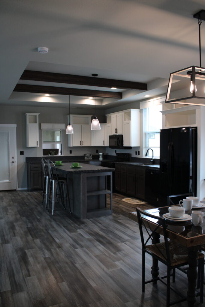 Modern kitchen with dark wood flooring, island with bar stools, black appliances, and white cabinets. Pendant and geometric lights create a cozy ambiance.