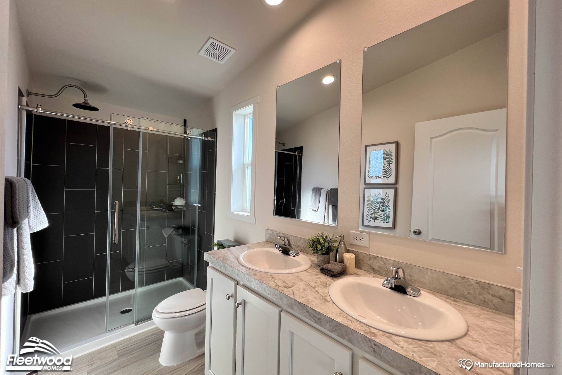 Modern bathroom with a sleek shower enclosed by glass doors, double sinks with polished faucets, and a marble countertop. The room is well-lit and minimalistic.