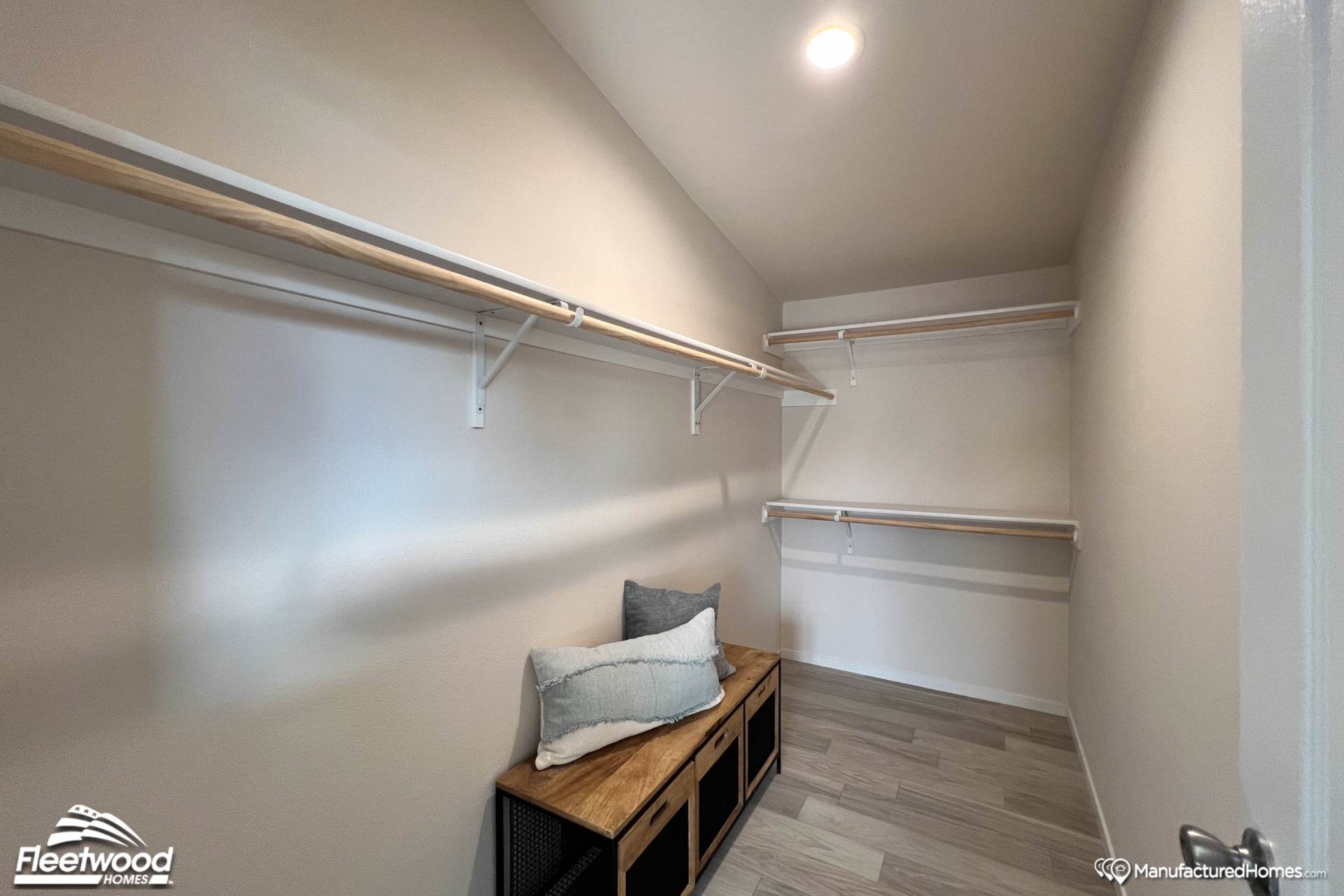 Spacious walk-in closet with light wood shelves and a ceiling light. A cushioned bench with black storage cubbies adds a cozy touch to the modern design.