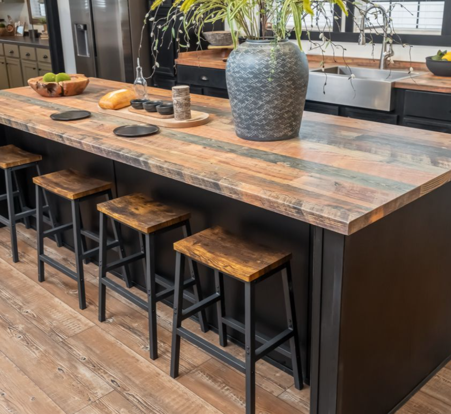 Rustic kitchen island with a wooden countertop and four matching stools. A large vase with leafy branches decorates the surface, creating a cozy atmosphere.