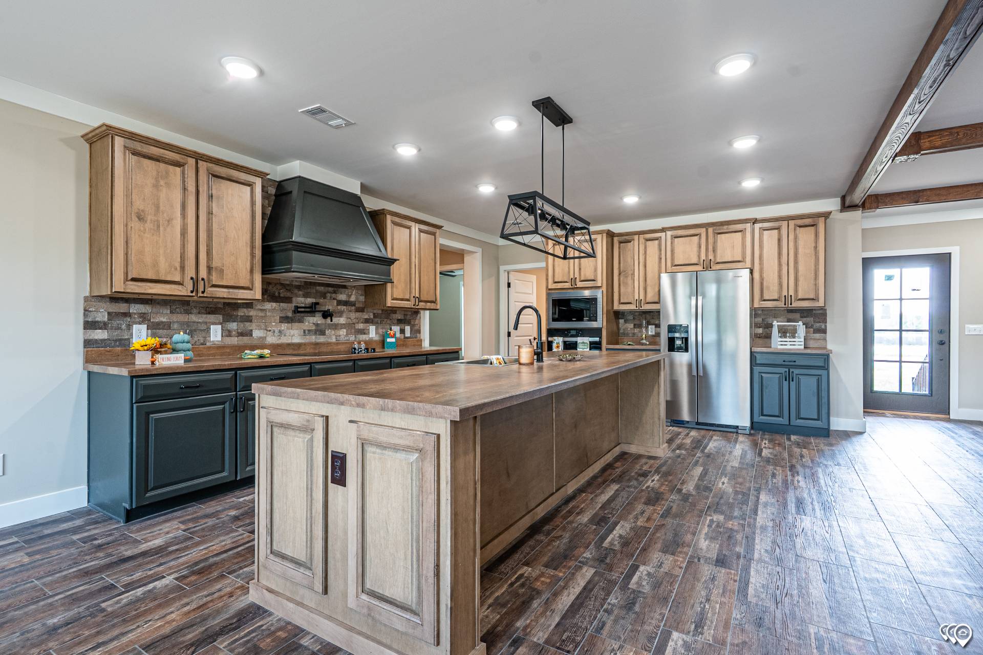 Spacious kitchen with rustic wood cabinets, a large central island, stainless steel appliances, and warm wood flooring. Bright and inviting atmosphere.