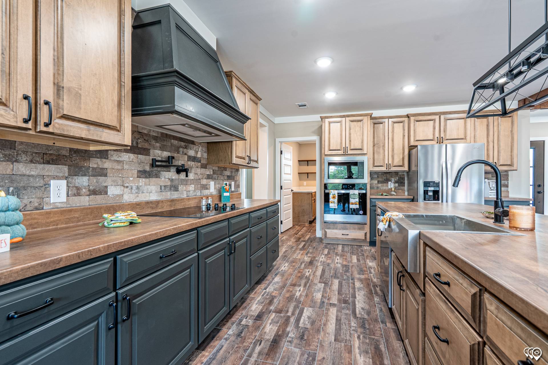 Spacious kitchen with wood cabinets, dark countertops, stainless steel appliances, and brick backsplash. Warm, inviting tone with ample lighting.