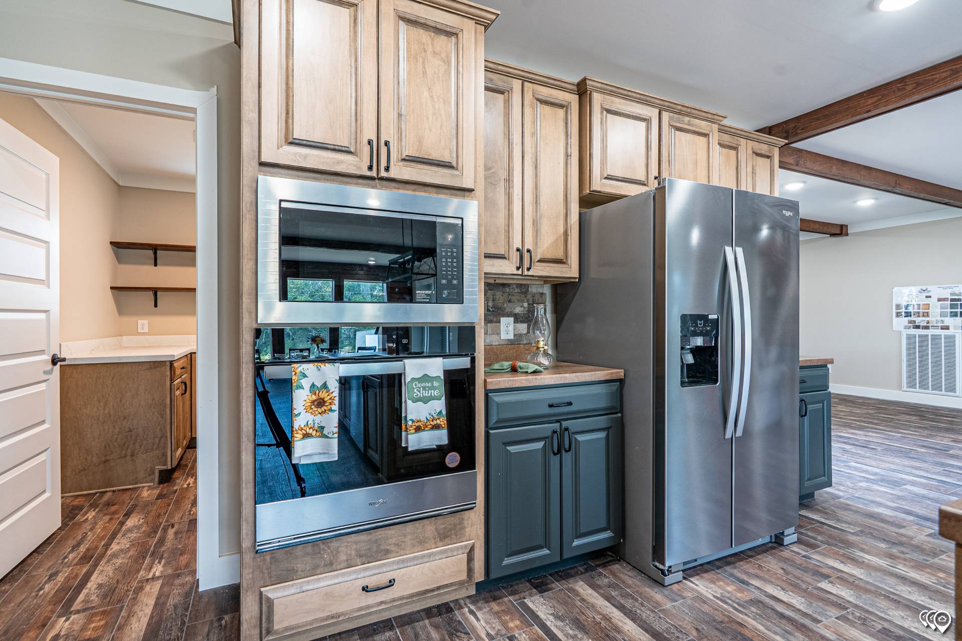 Modern kitchen with stainless steel refrigerator, wall oven, beige and blue cabinets, and wood floor. Bright and spacious with open layout.