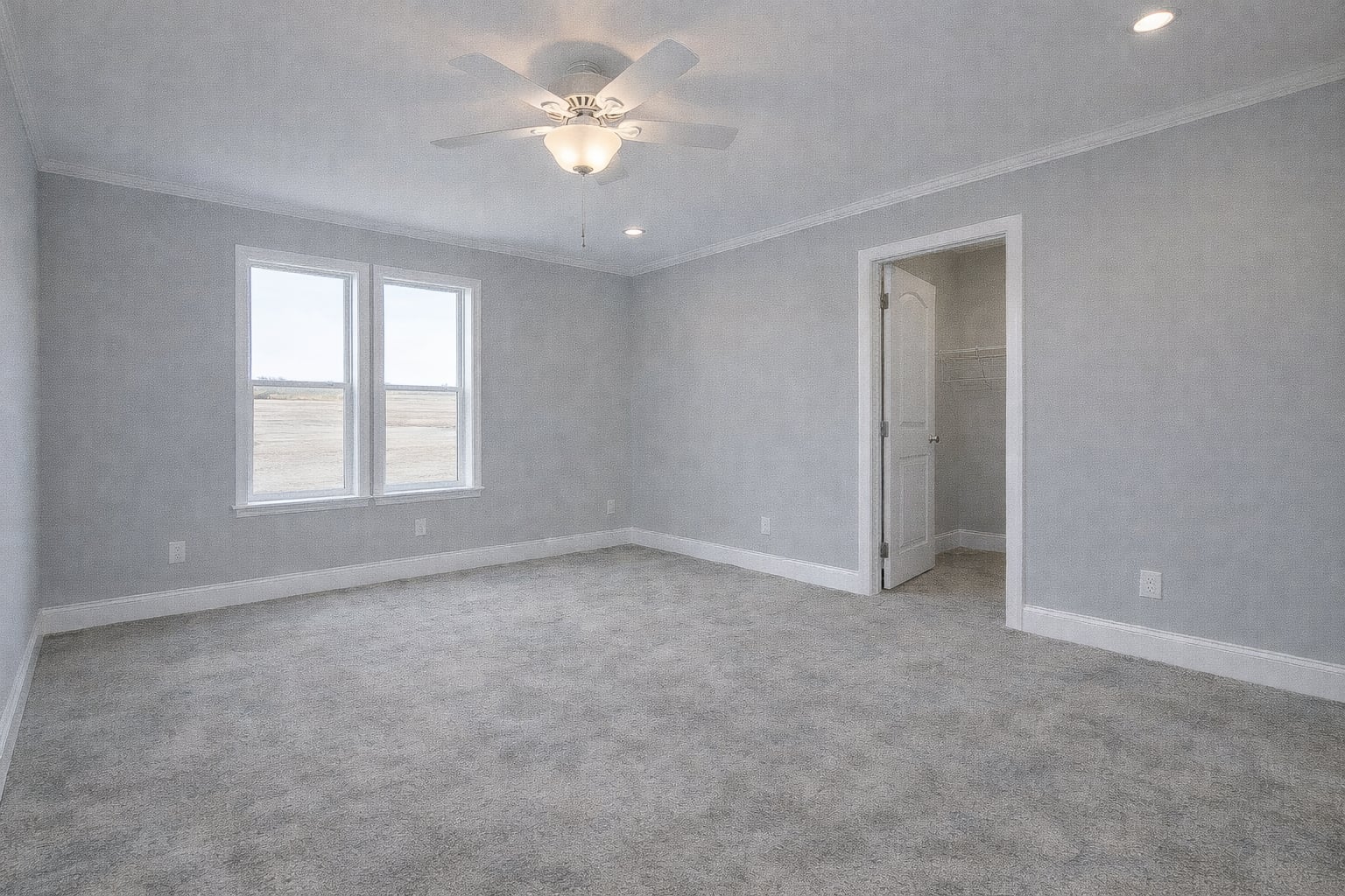 Spacious empty room with light gray walls and carpet, ceiling fan with light, and two large windows. Open door leads to a closet. Bright and airy.