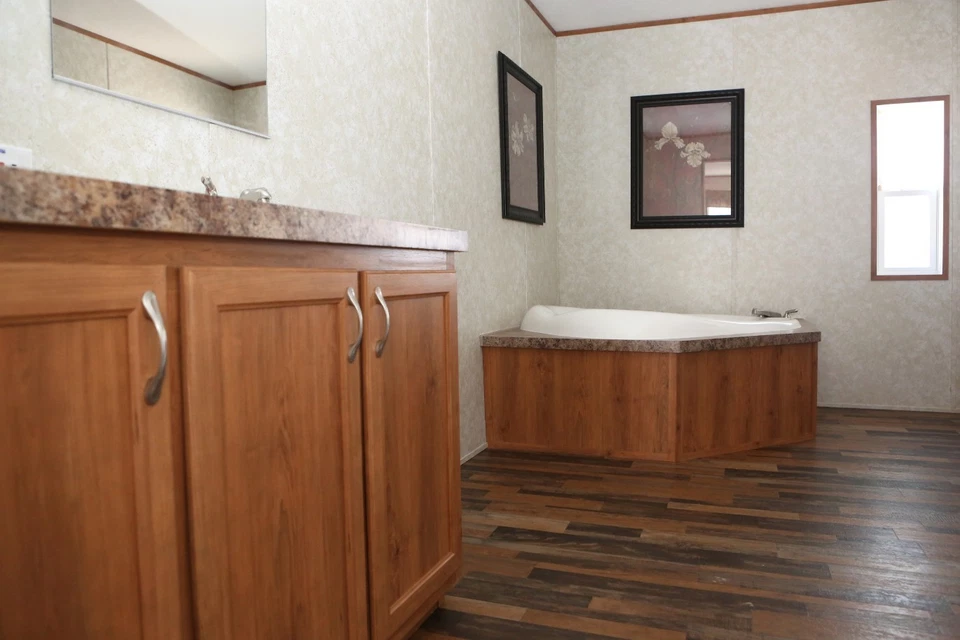 Spacious bathroom with wooden cabinets, a large corner bathtub, and floral artwork. Warm tones and natural light create a cozy and inviting atmosphere.