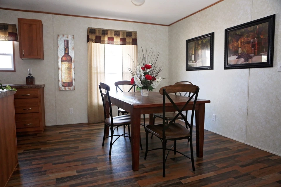 A cozy dining room with a wooden table set for four, featuring a vase of red and white flowers. Warm lighting and framed art create an inviting atmosphere.
