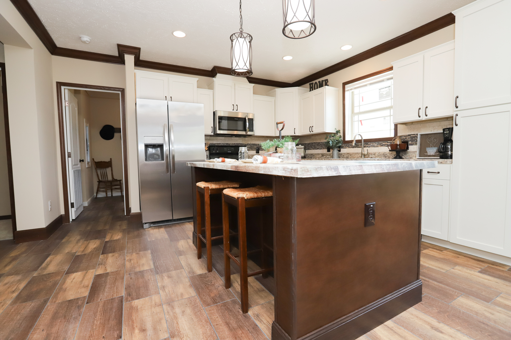 Modern kitchen with white cabinets, stainless steel appliances, and a wooden island with two stools. Warm lighting creates a cozy atmosphere.