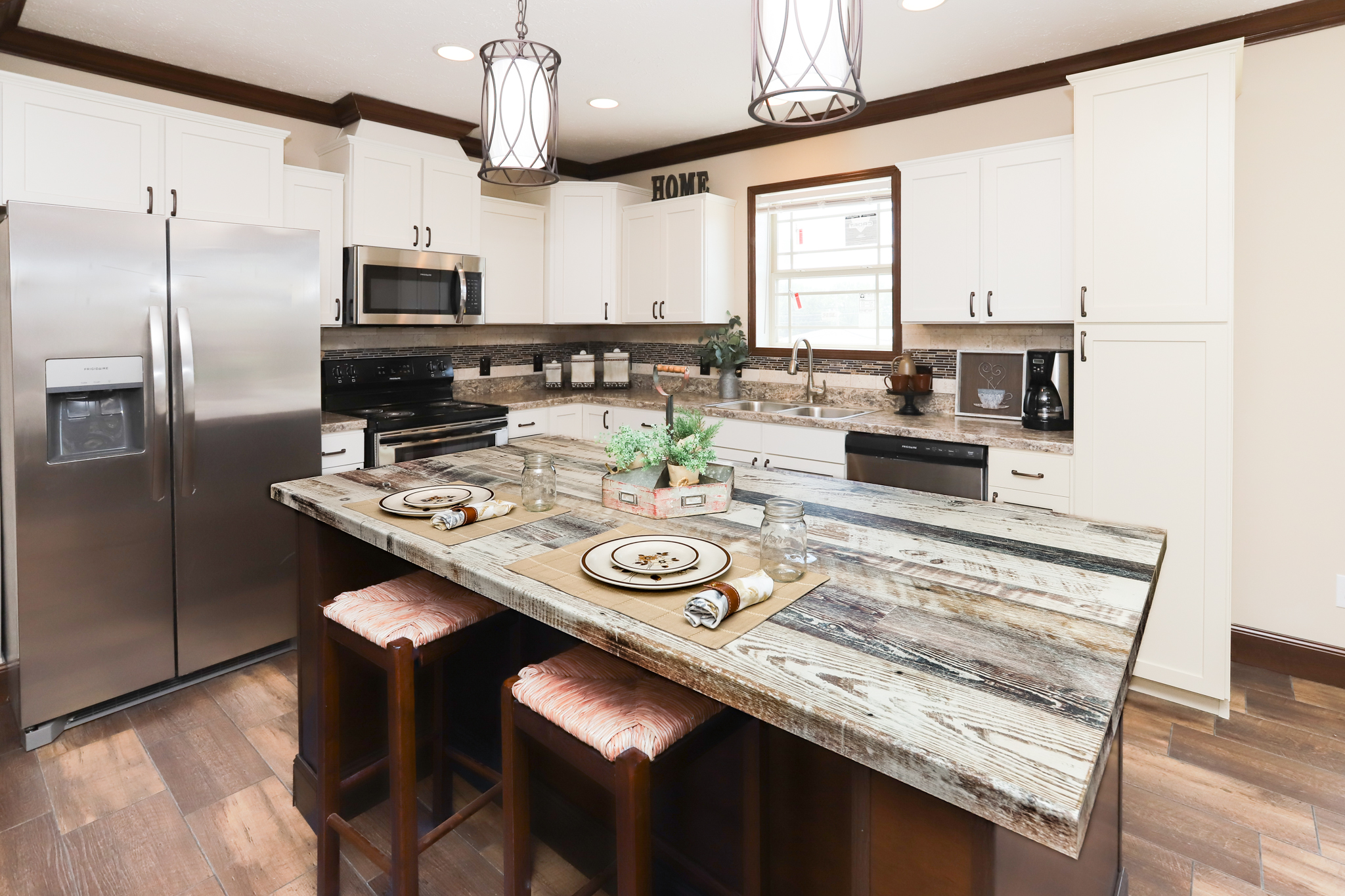 Modern kitchen with white cabinets and stainless steel appliances. A rustic island with two stools is set with plates and napkins, creating a cozy atmosphere.