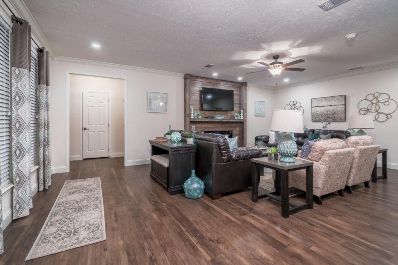 Stylish living room with wooden floor, brown leather sofa, patterned armchairs, and decorative vases. A TV and fireplace create a cozy ambiance.