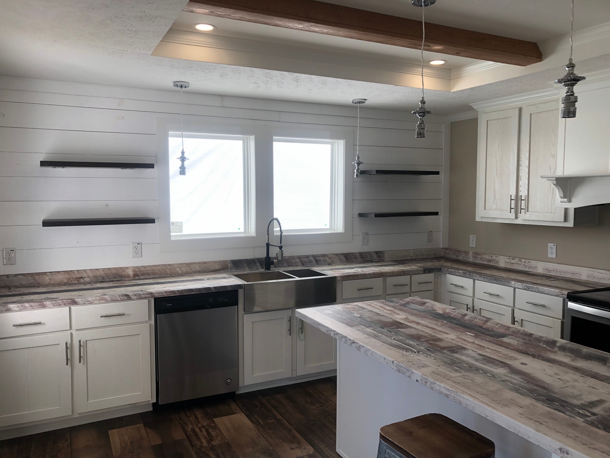 Modern kitchen with white cabinetry, rustic wooden countertops, and open shelving. Features a farmhouse sink, stainless steel dishwasher, and warm lighting.