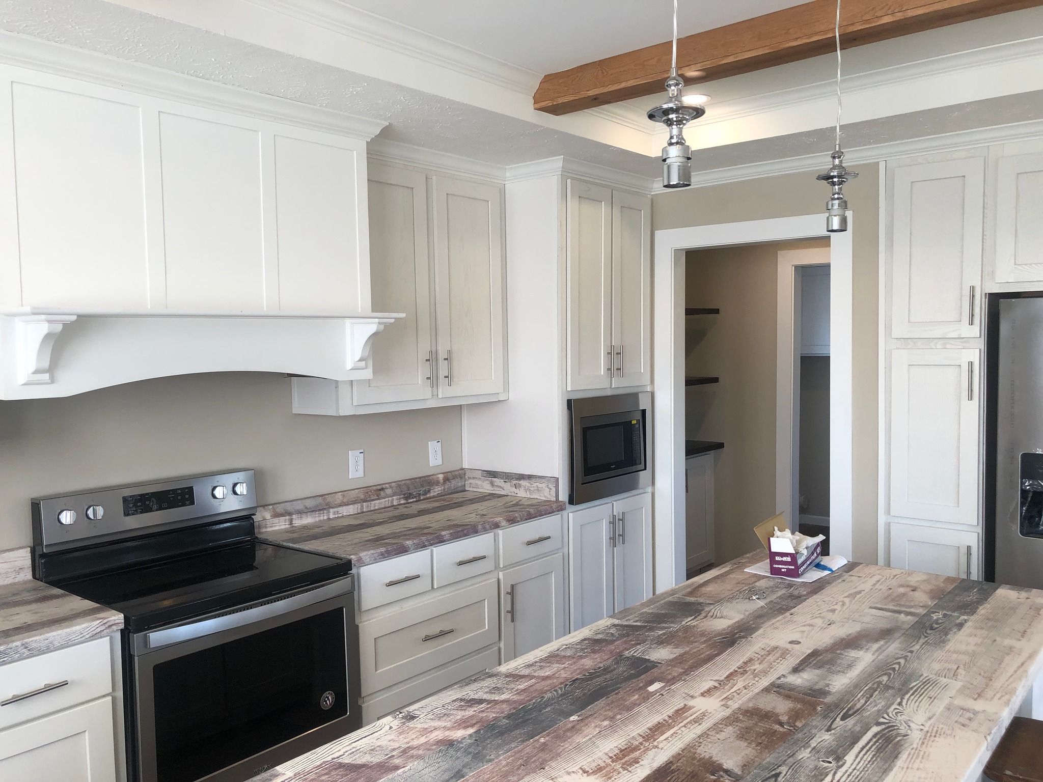Modern kitchen with white cabinets and rustic wood countertops. Stainless steel appliances, including a stove and fridge. Exposed wooden beam and pendant lights add charm.