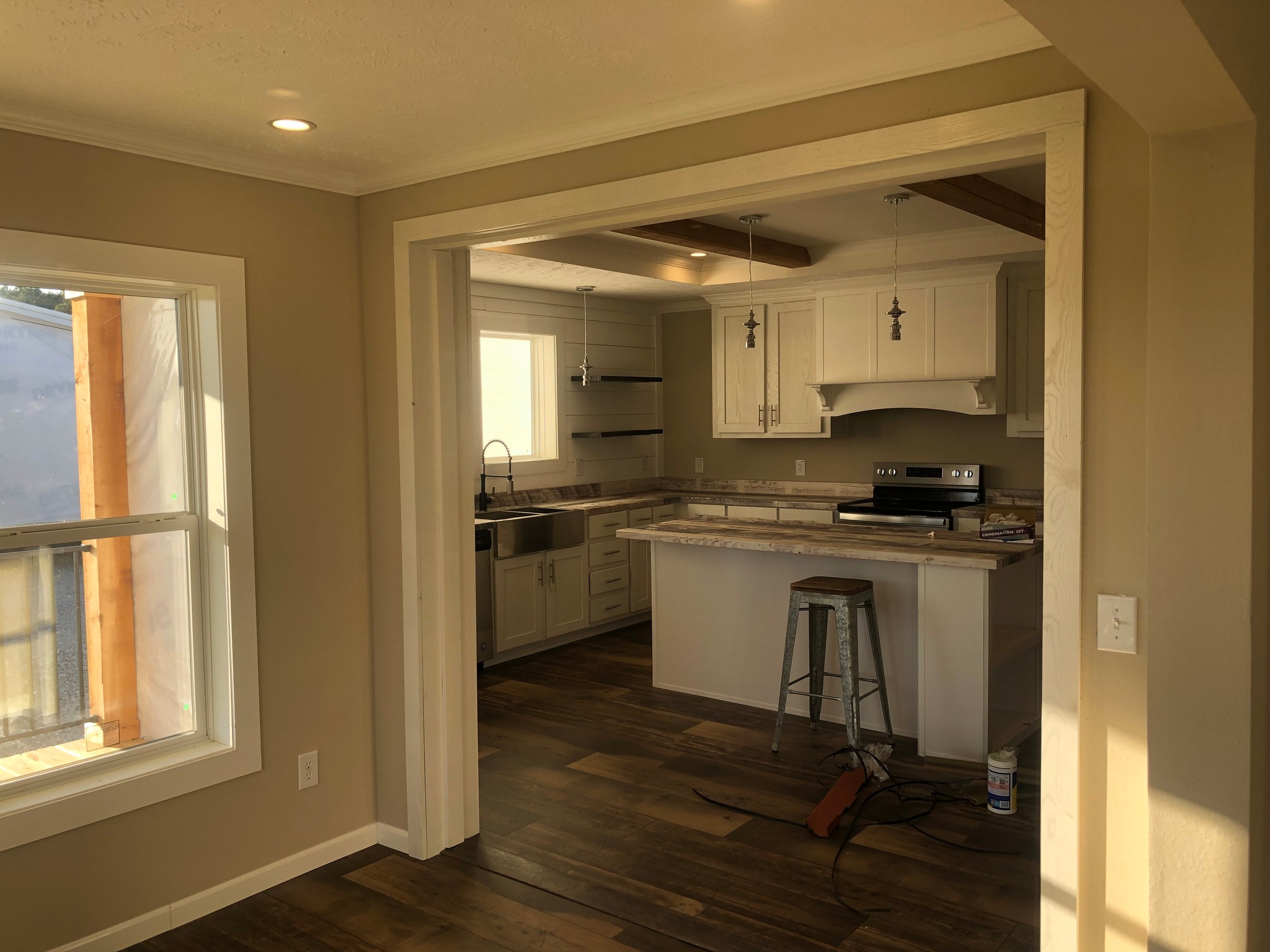 A cozy kitchen with white cabinets, wood floor, and pendant lights. A window lets in natural light, creating a warm, inviting atmosphere.