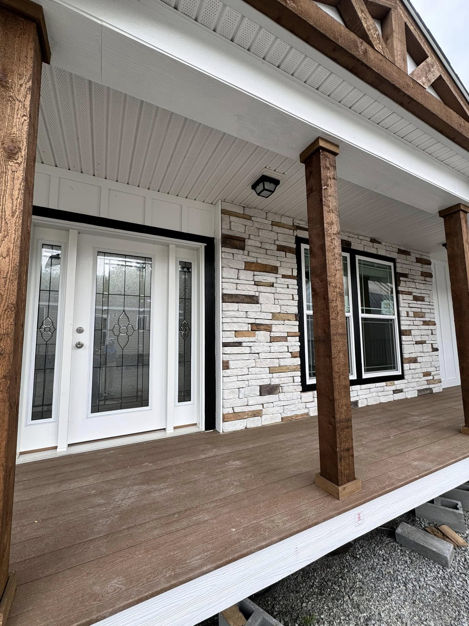 A porch with wooden beams and a textured stone wall. It features a glass-paneled double door and two windows, creating a rustic and inviting feel.
