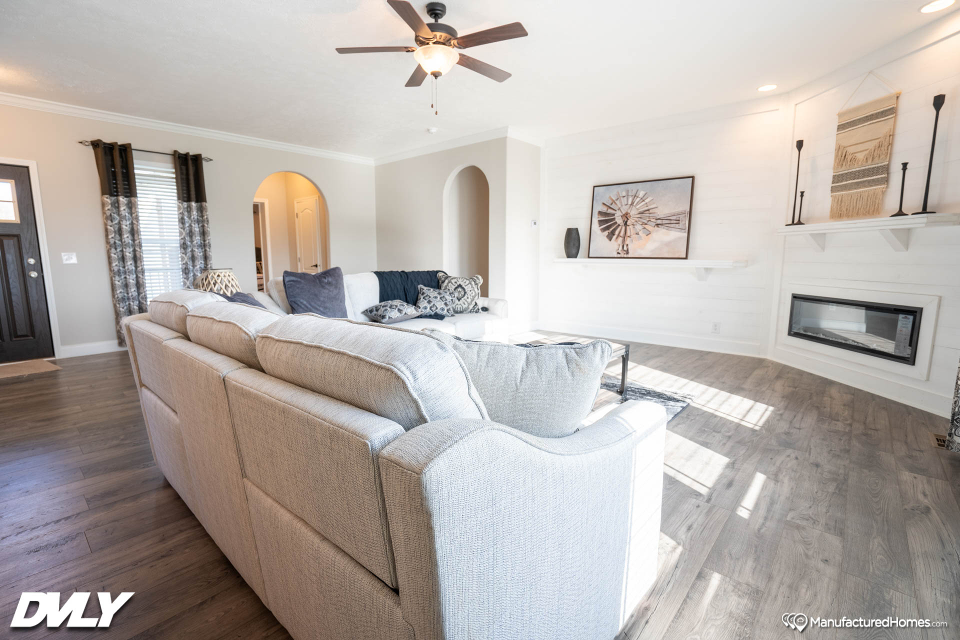 Spacious living room with a beige sectional sofa, patterned cushions, and a ceiling fan. Decor includes Southwest art, a modern fireplace, and wood floors. Bright and inviting.