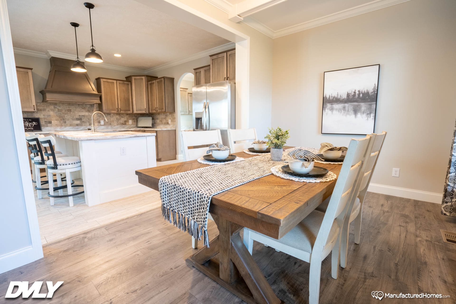 A cozy dining area with a wooden table set for four, white chairs, and a checkered runner. The background features a modern kitchen and serene wall art.