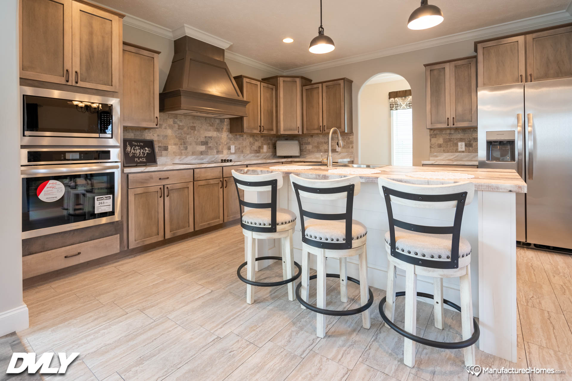 Modern kitchen with wooden cabinets, stainless steel appliances, and a center island with three stools. Warm lighting and a cozy atmosphere.