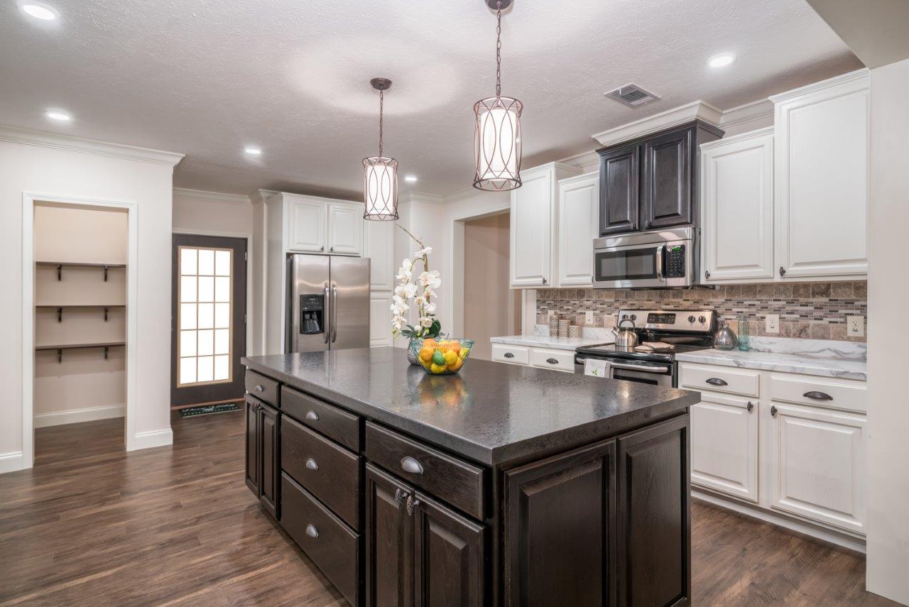Bright kitchen with dark wood island, white cabinets, stainless steel appliances, and pendant lights. A bowl of fruit and flowers add a fresh touch.