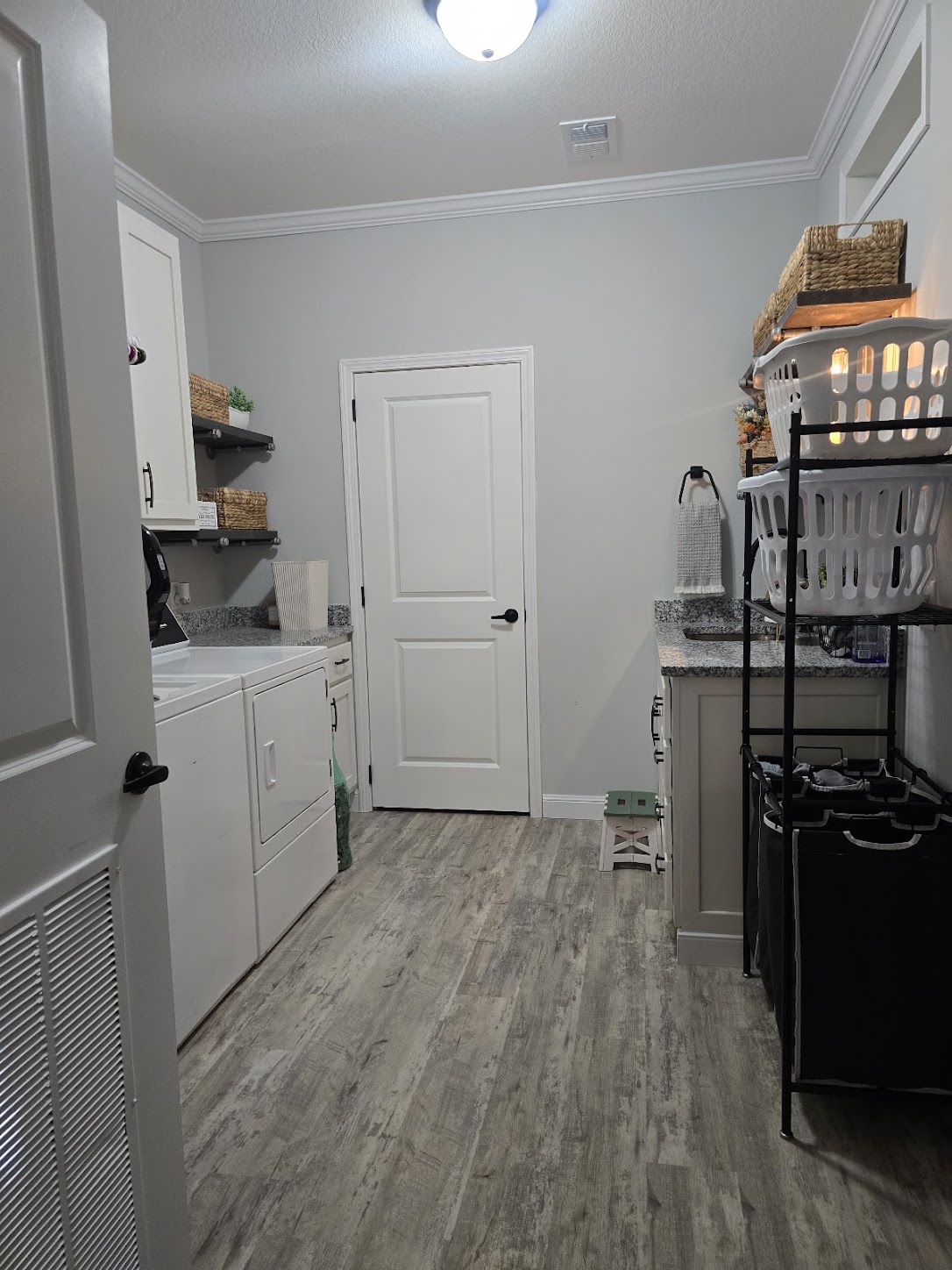 Laundry room with wood flooring, white cabinets, and gray countertops. Washer and dryer on the left, baskets on shelves, light fixture above.