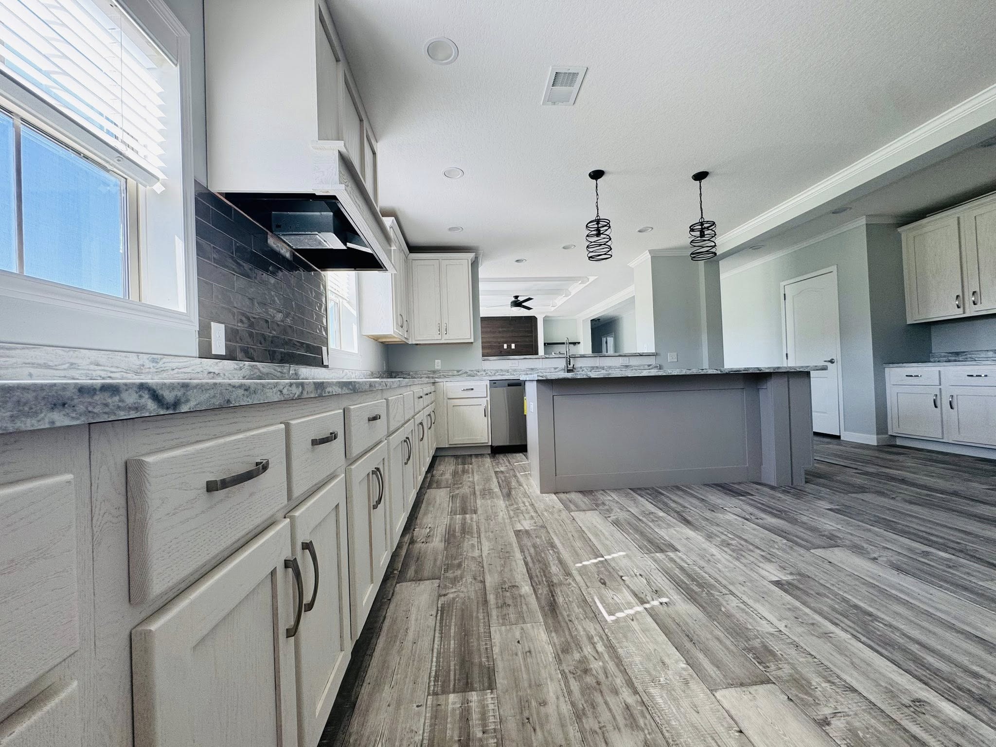 Spacious modern kitchen with light wood cabinets, marble countertops, and a long island. Pendant lights hang from the ceiling, creating an airy feel.