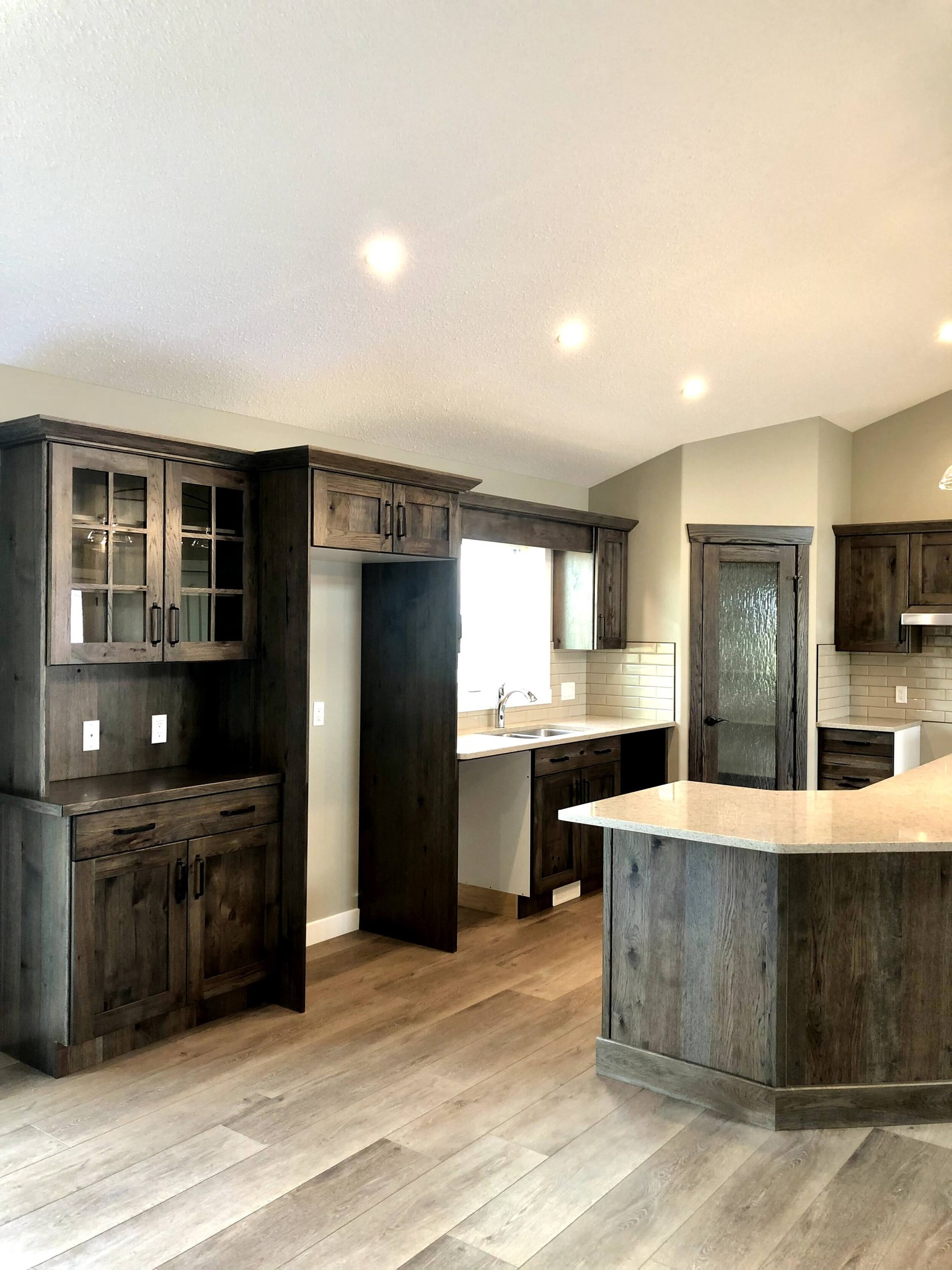 Spacious kitchen with rustic dark wood cabinets, a central island, beige walls, and light wooden flooring. Bright and modern with a cozy atmosphere.