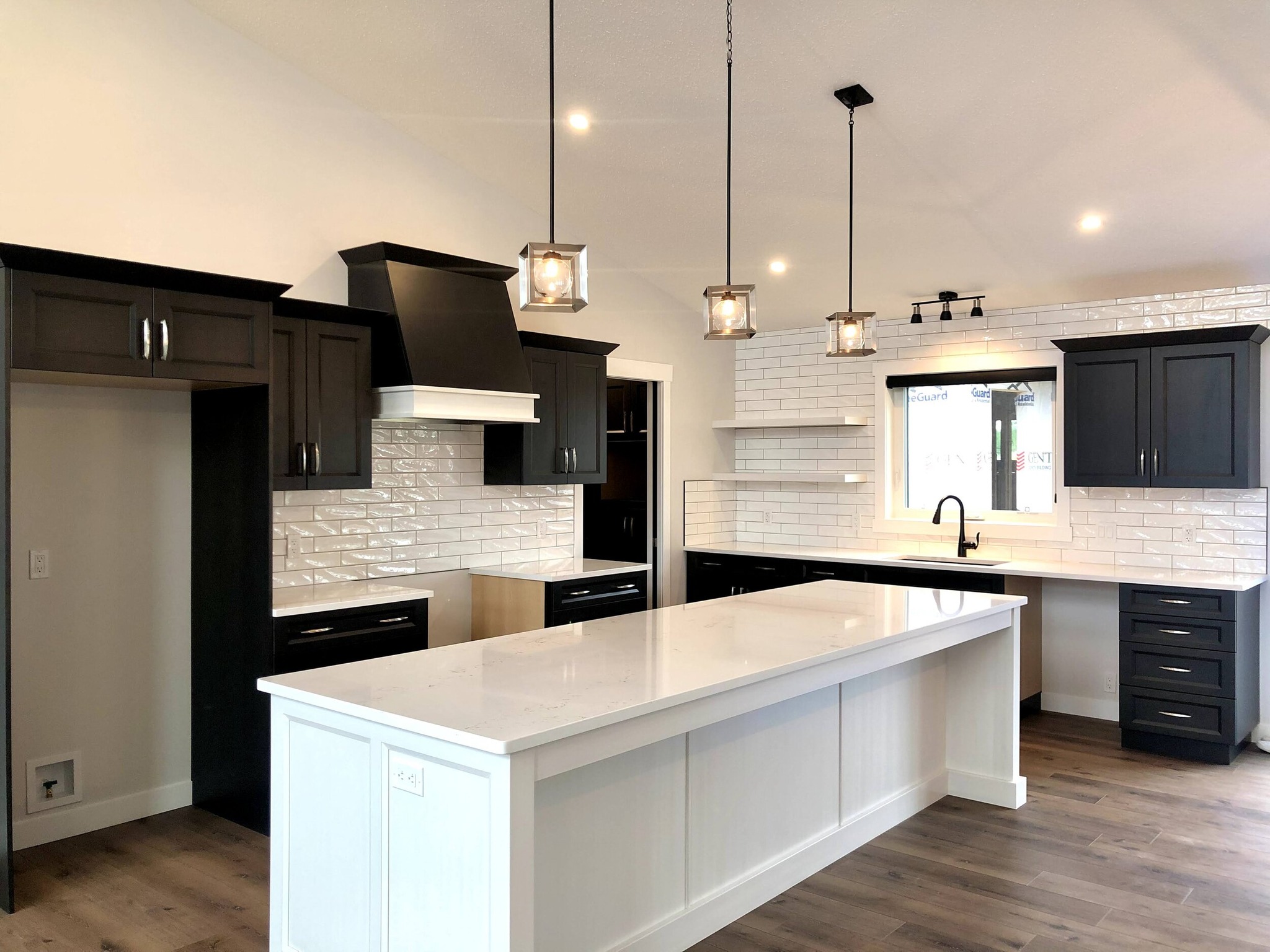 Modern kitchen with sleek black cabinets, white quartz countertops, and subway tile backsplash. Pendant lights hang over a large island, creating a bright, inviting space.