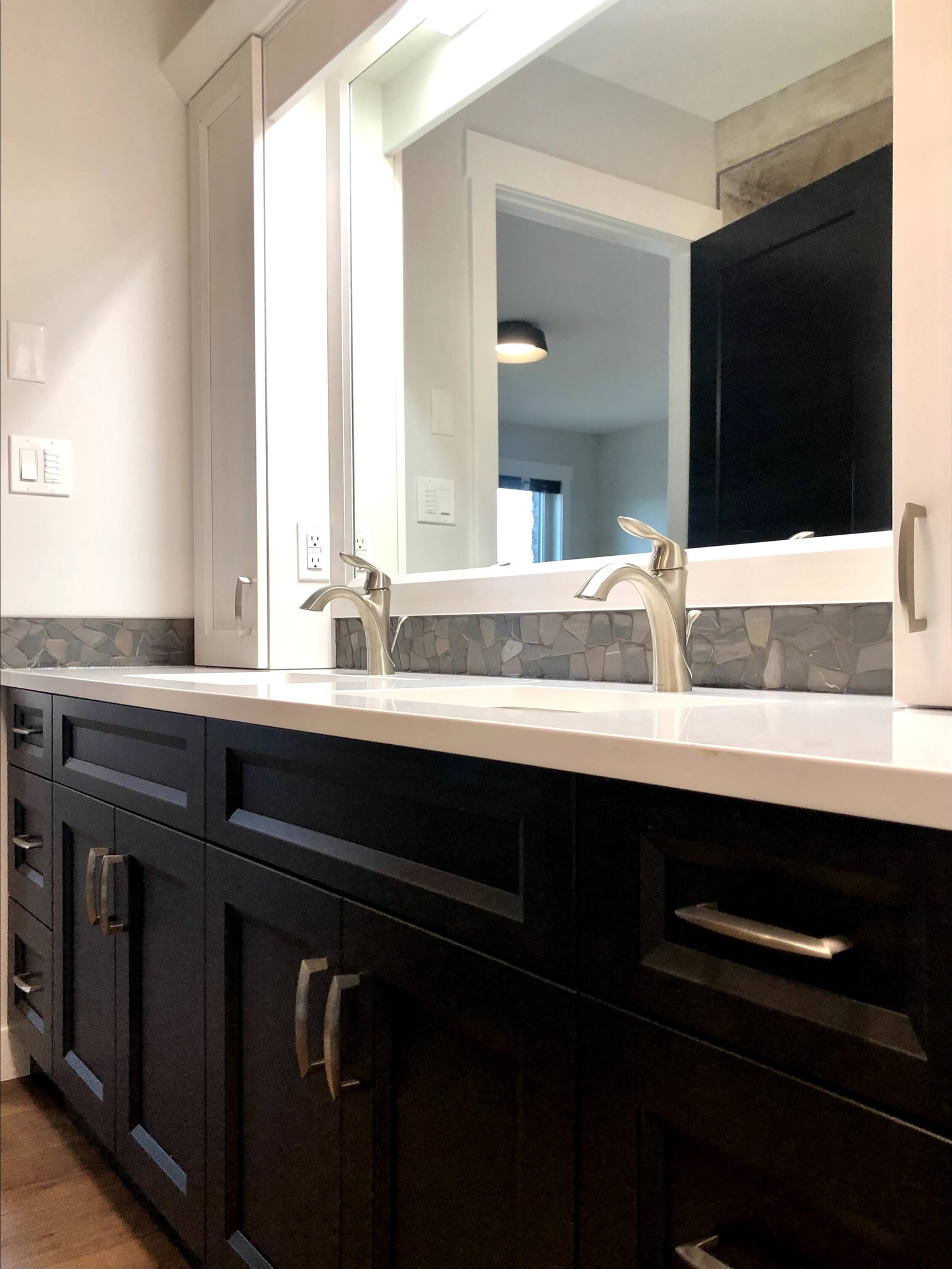 Modern bathroom with a sleek double sink and elegant chrome faucets. Dark cabinetry contrasts with a light counter, creating a clean, sophisticated look.