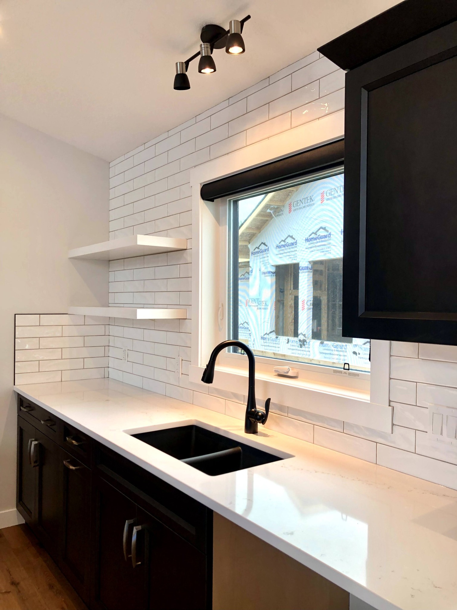 Modern kitchen with white subway tile backsplash, black countertop, and sink. Under-cabinet lighting and open shelves create a sleek, bright ambiance.