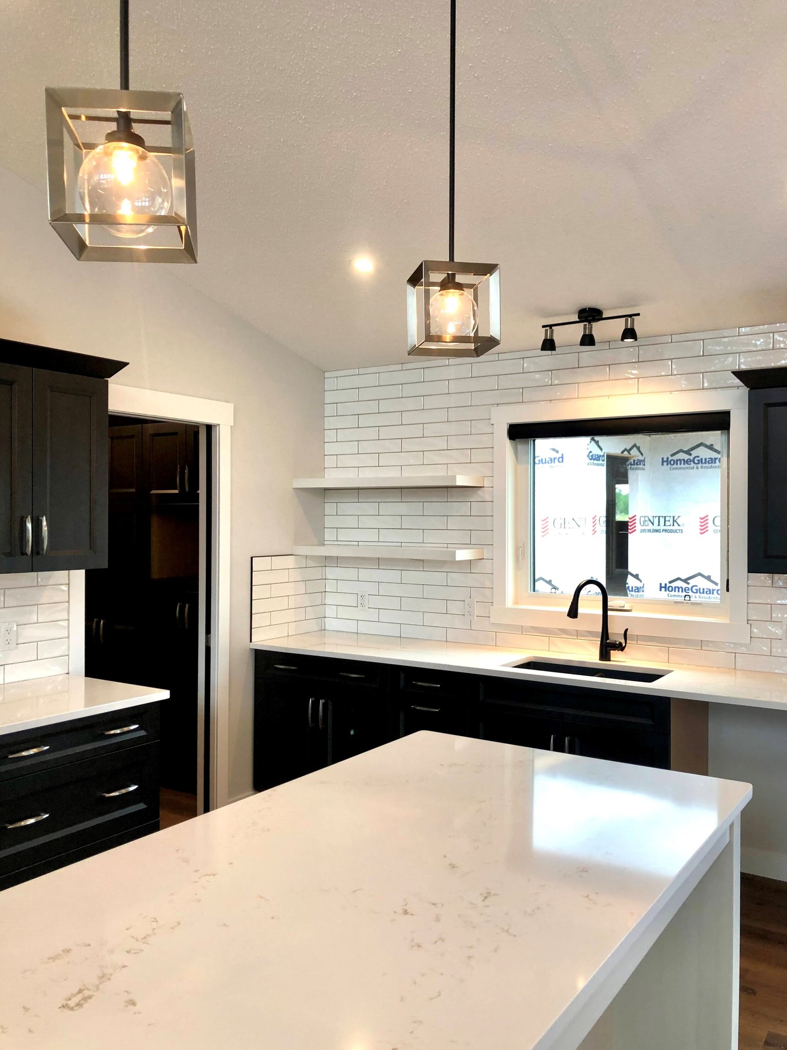 Modern kitchen with black cabinets, white countertops, and subway tile backsplash. Pendant lights hang above the island, creating a sleek, bright space.