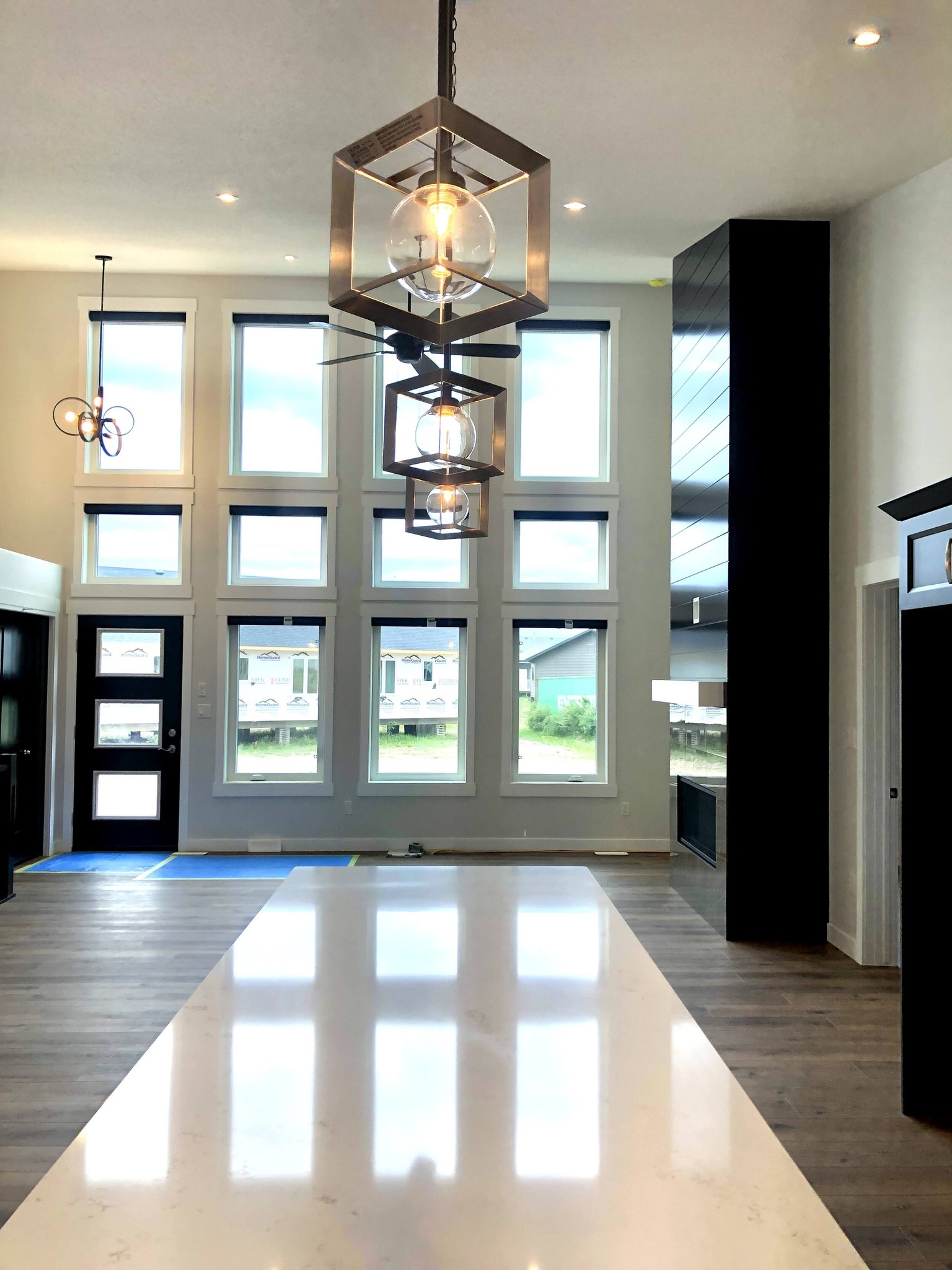 Spacious modern interior with large grid windows and high ceiling. Features geometric pendant lights, wooden floors, and a sleek minimalist design.