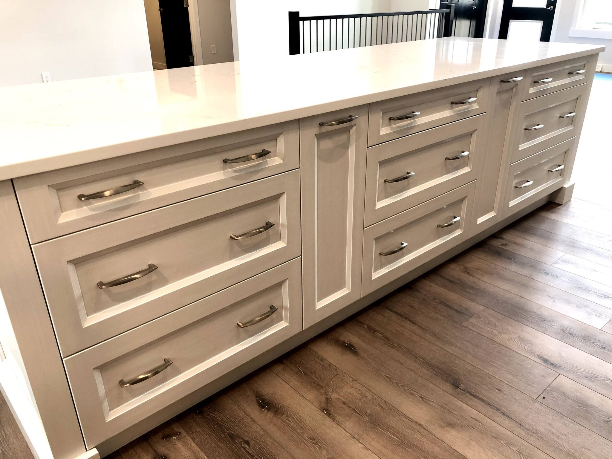 A modern kitchen island with a sleek white countertop and cream-colored drawers featuring silver handles, set against a light wood floor.