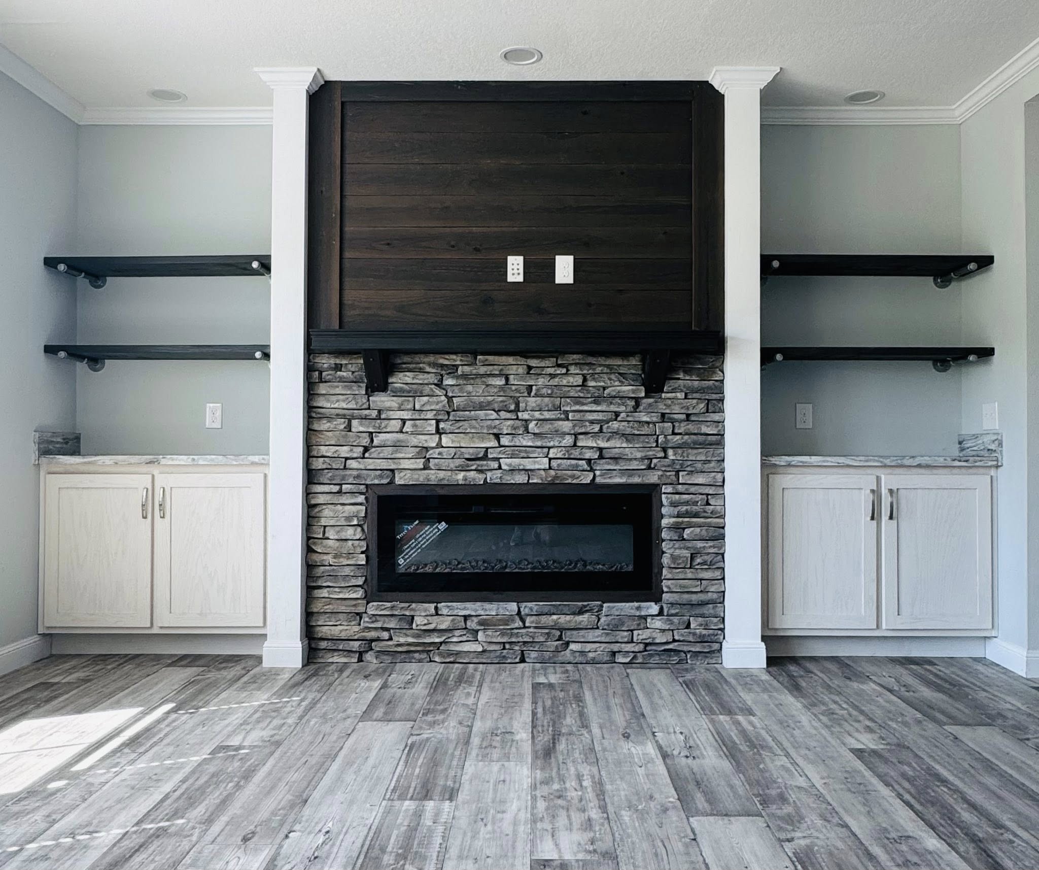 Modern living room with a dark stone fireplace and hardwood floors. Flanked by white cabinets and black shelves, the atmosphere is sleek and cozy.